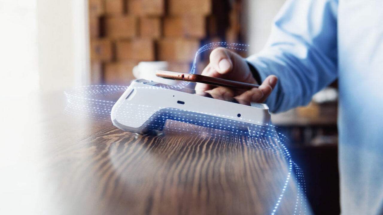 Close‐up of a person’s hands using a handheld device making a digital payment.